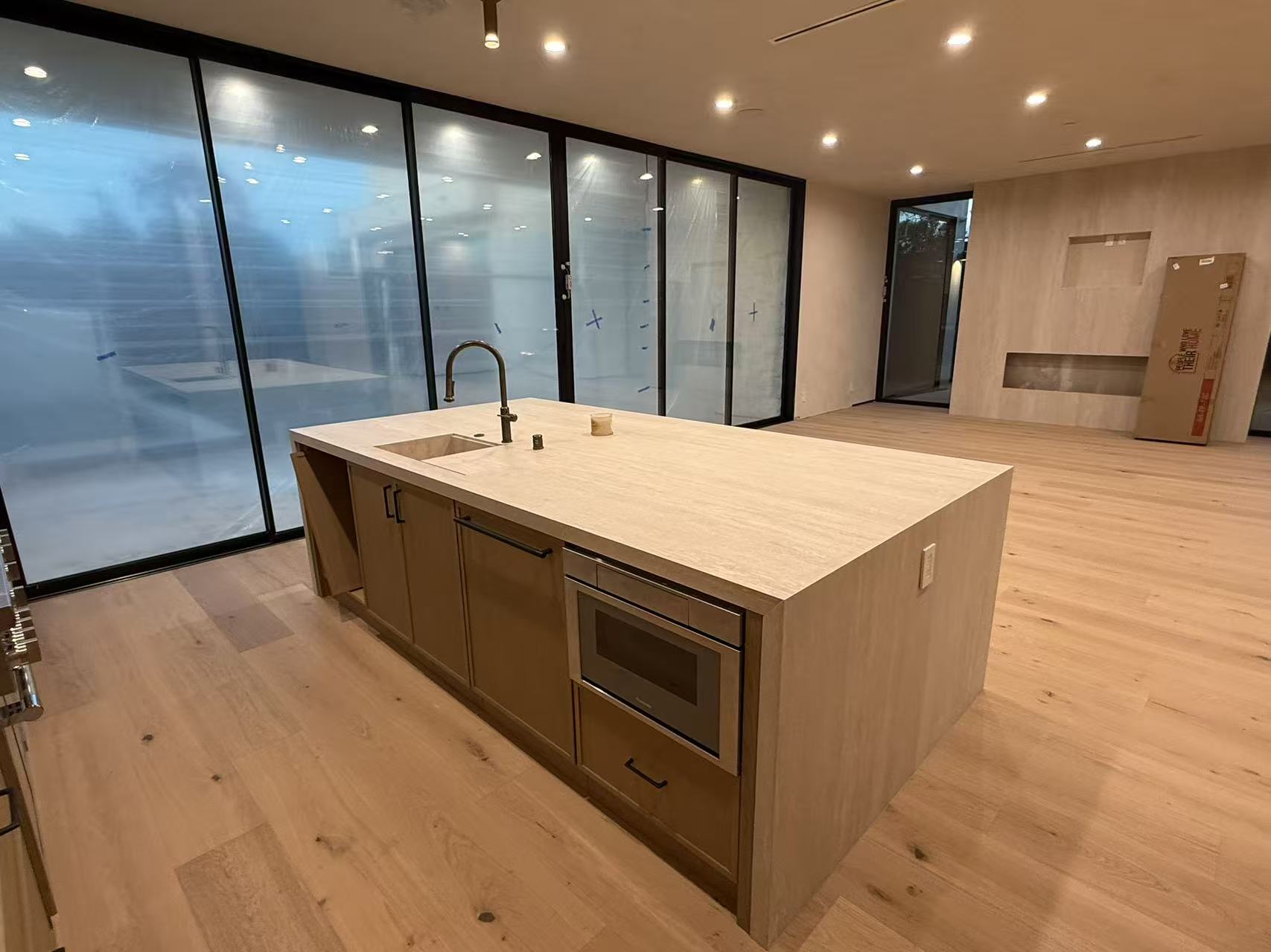 Open kitchen with travertine island, oak cabinetry and floor-to-ceiling black-frame glass wall to courtyard