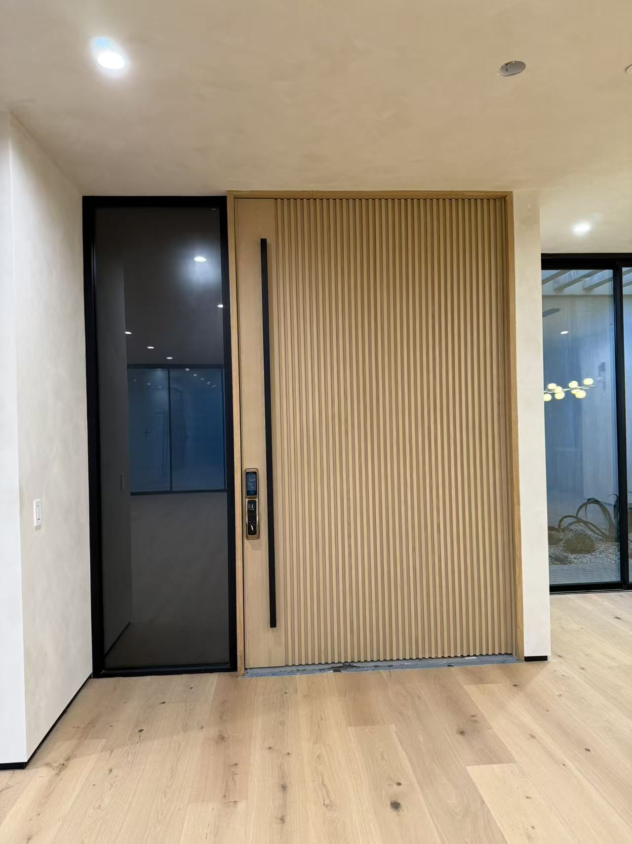 Foyer with fluted oak pivot door and slim-frame black aluminum sidelight