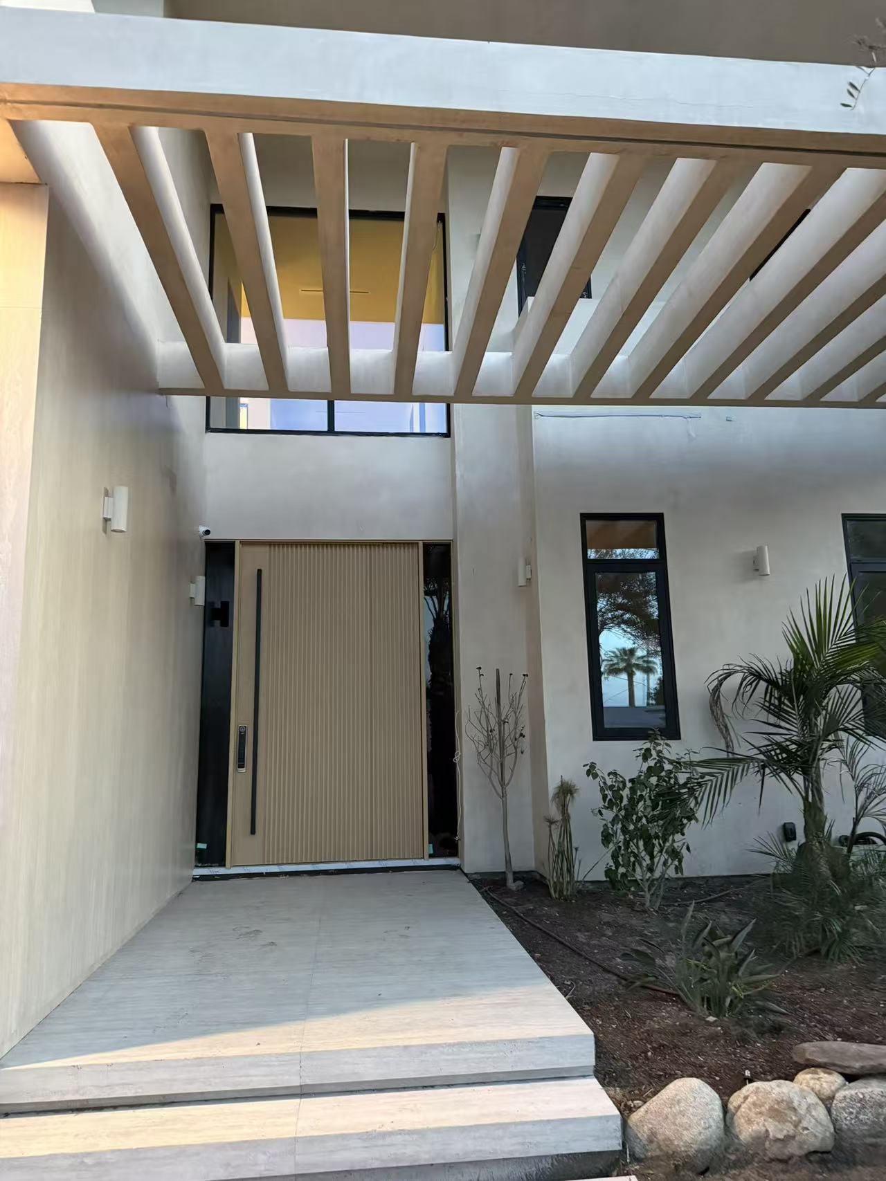 Pivot entry door in white oak with slim sidelight and floating pergola overhead